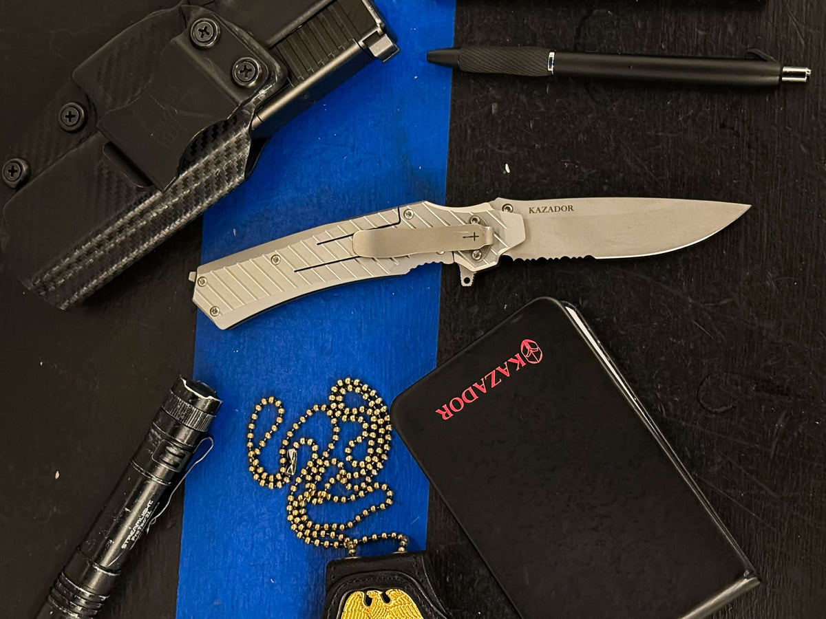 Huntsman border knife, view from frame-lock side eight open blade showing its silver, stone-washed finish . In the center of  pocket notebook, next to a bad, next to a flash light and on top left of knife a gun holster.